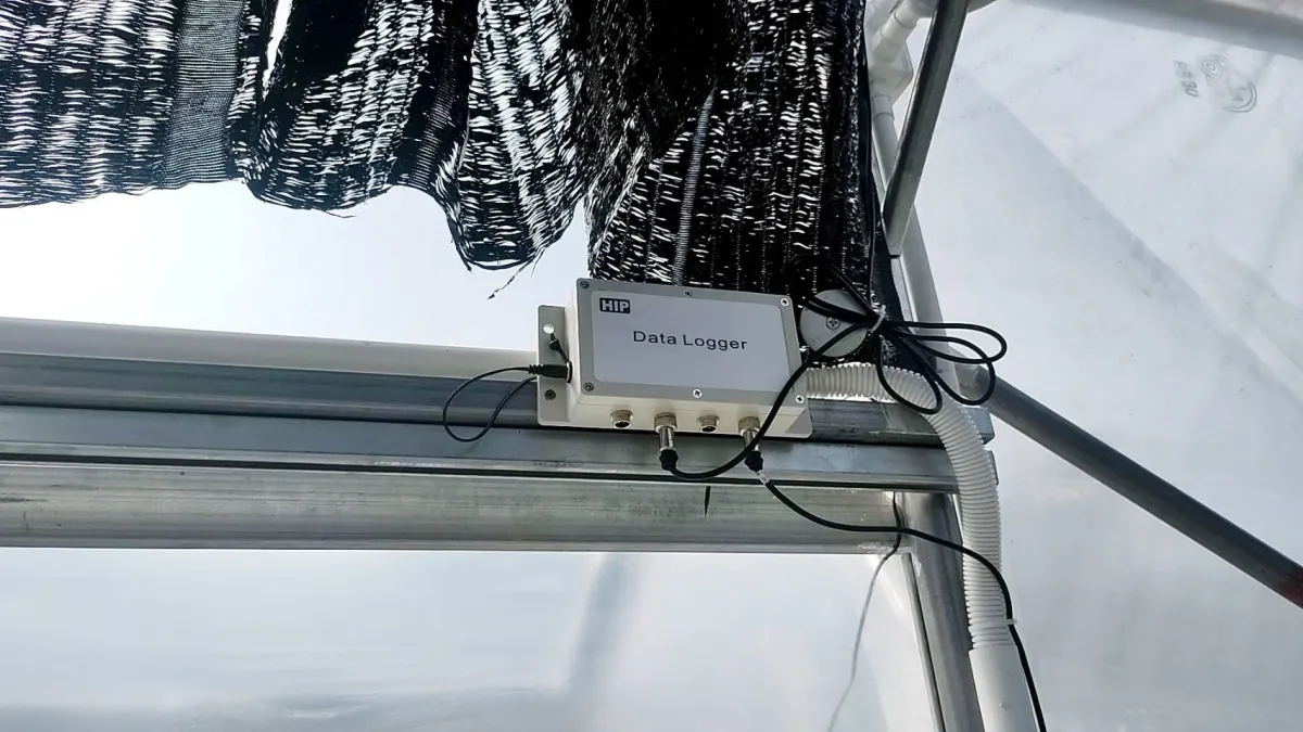 A data logger mounted on a greenhouse frame under the shade net